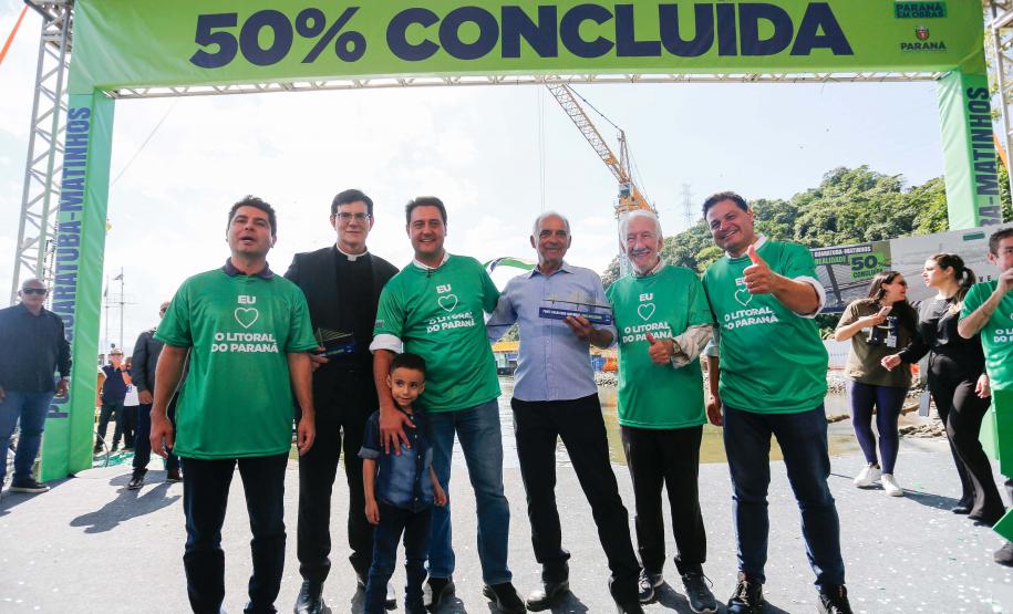 homens em frente a faixa de "50% concluída" da ponte